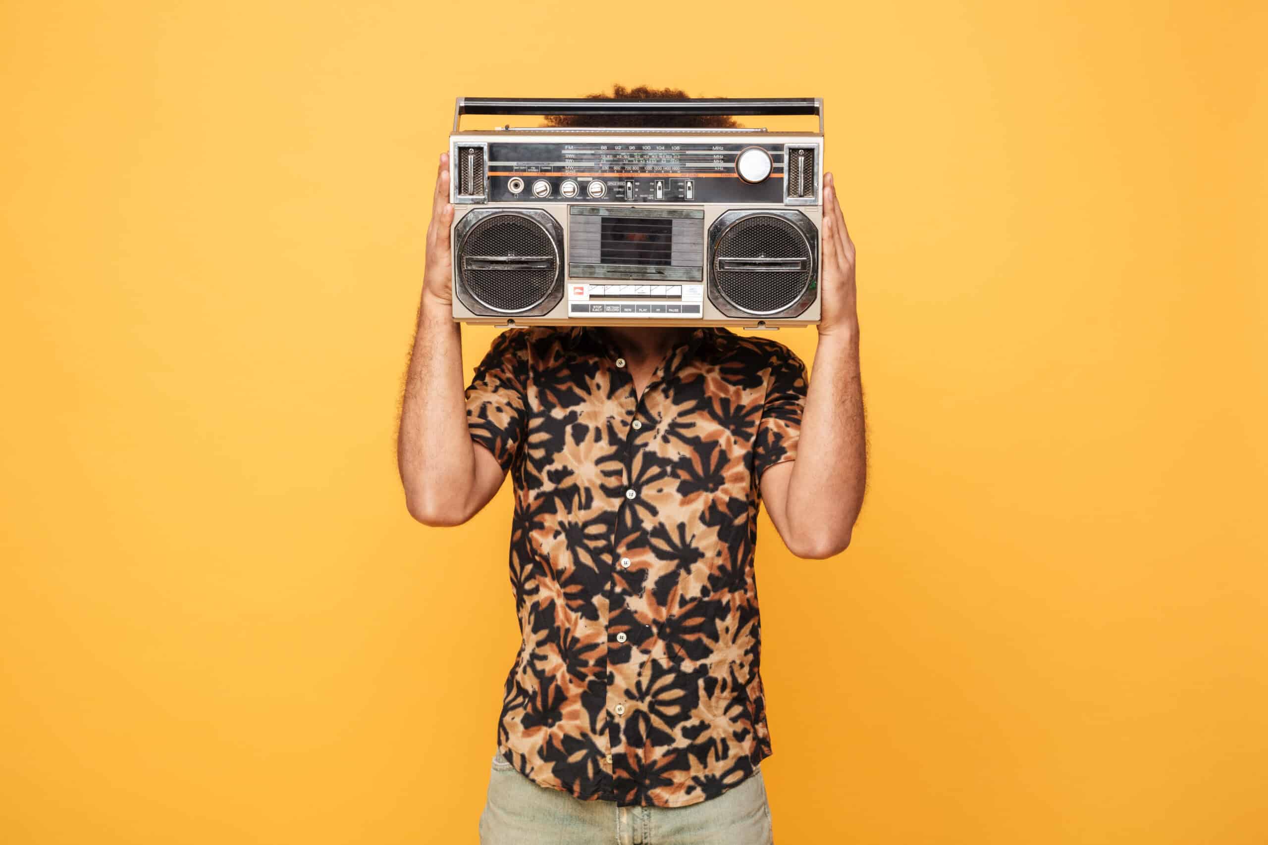 Young man covering his face with radio isolated over yellow background.