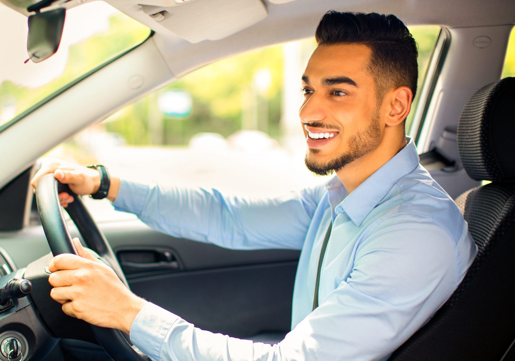 Middle-eastern businessman driving car, going on business trip, side view, copy space. Happy arab man in stylish outfit going to business meeting or to office, driving his luxury car