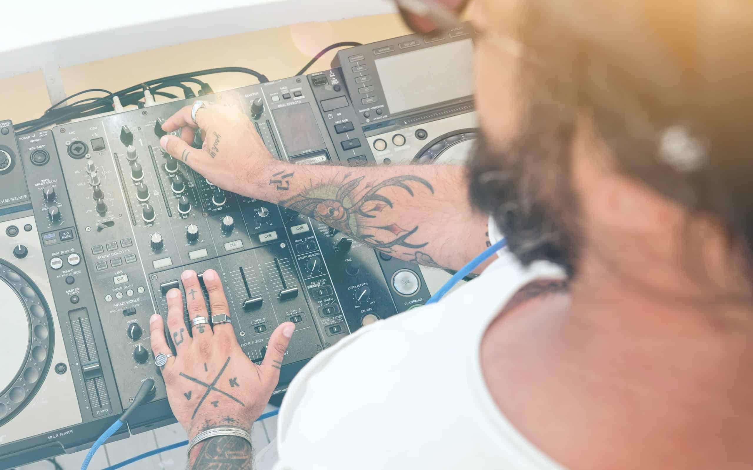 From above view of anonymous male DJ with tattoos working on controller at disco party